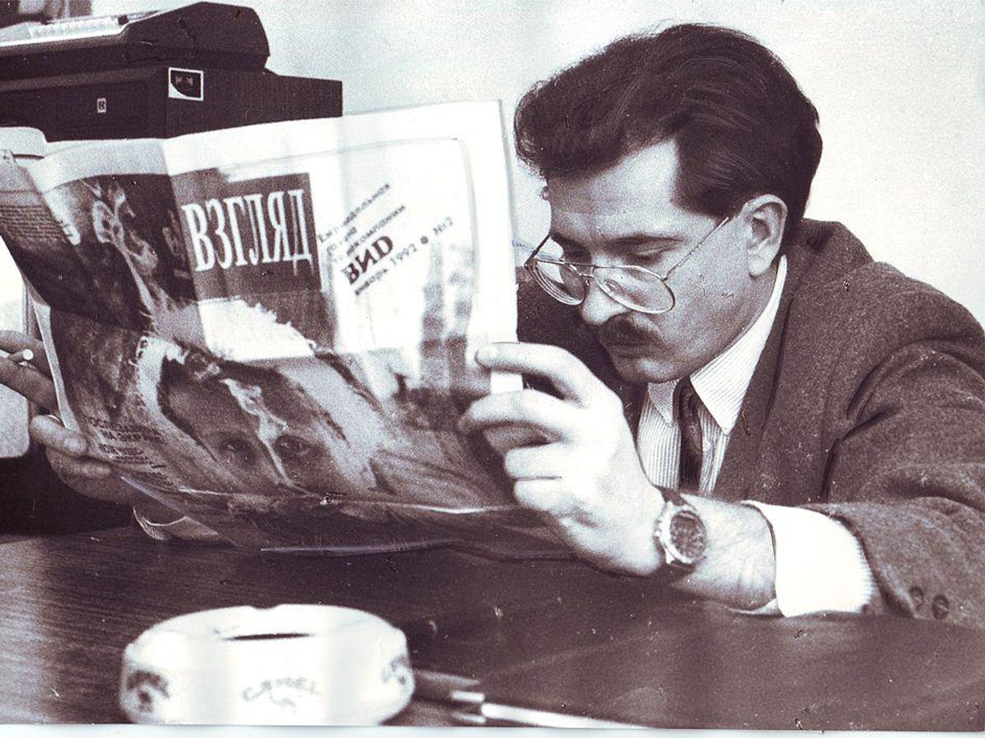 Black-and-white photo of TV host Vladislav Listyev reading Novy Vzglyad weekly