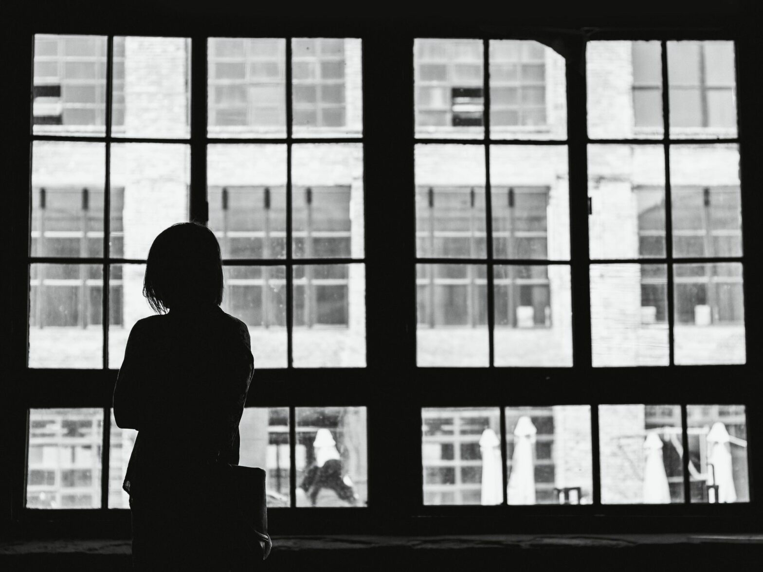 Black and white photo showing someone looking by the widow