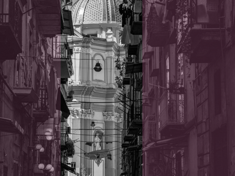 black and white photograph of a woman walking down a Neapolitan street, towards a large church.