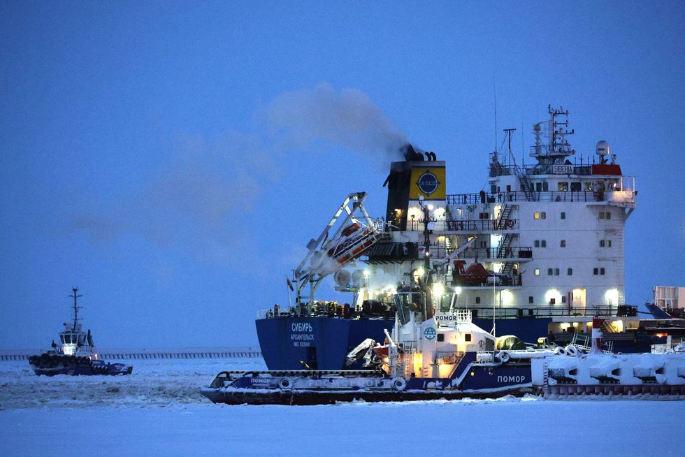 Boats and heavy machinery dock in an icy landscape, illuminated at dusk by only their own lights