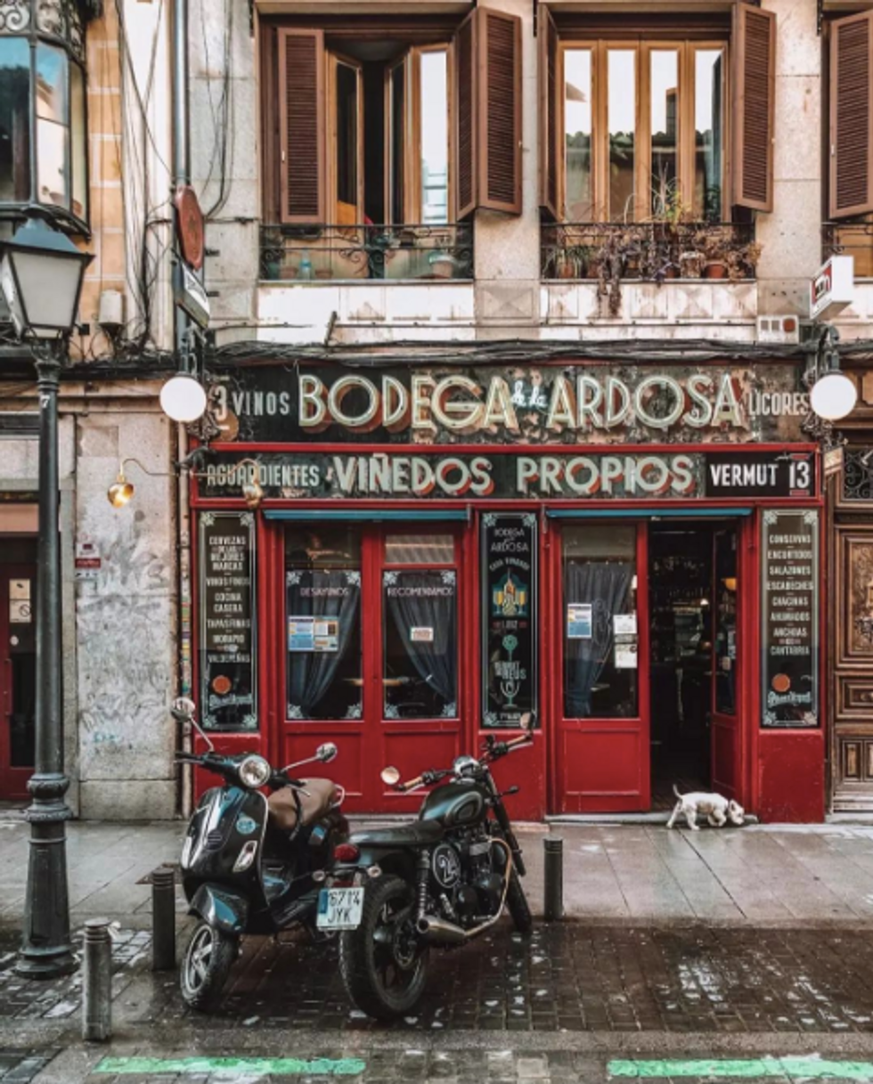 Bodega de la Ardosa with two motorcycles parked outside​ and a door in the doorway