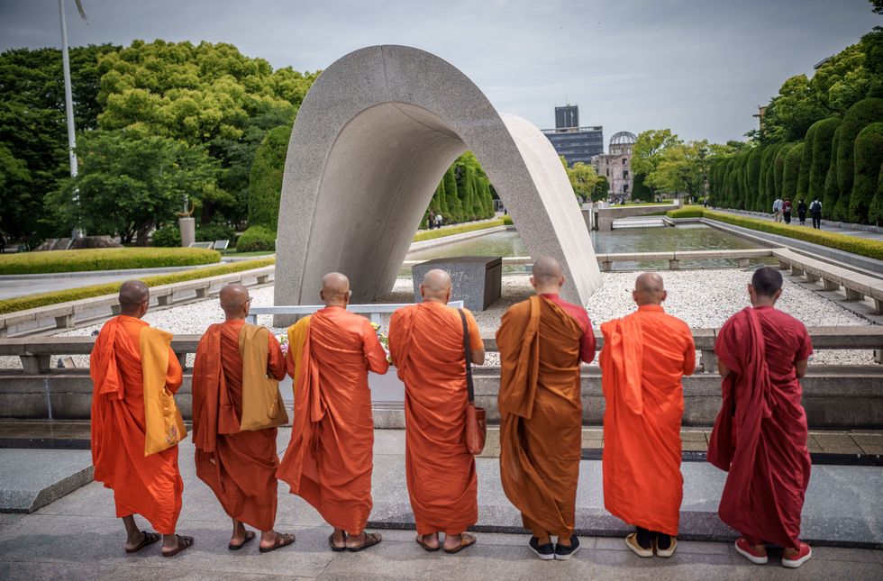 Buddhist monks stand in front of the Kenothap Memorial in Hiroshima Peace Memorial Park