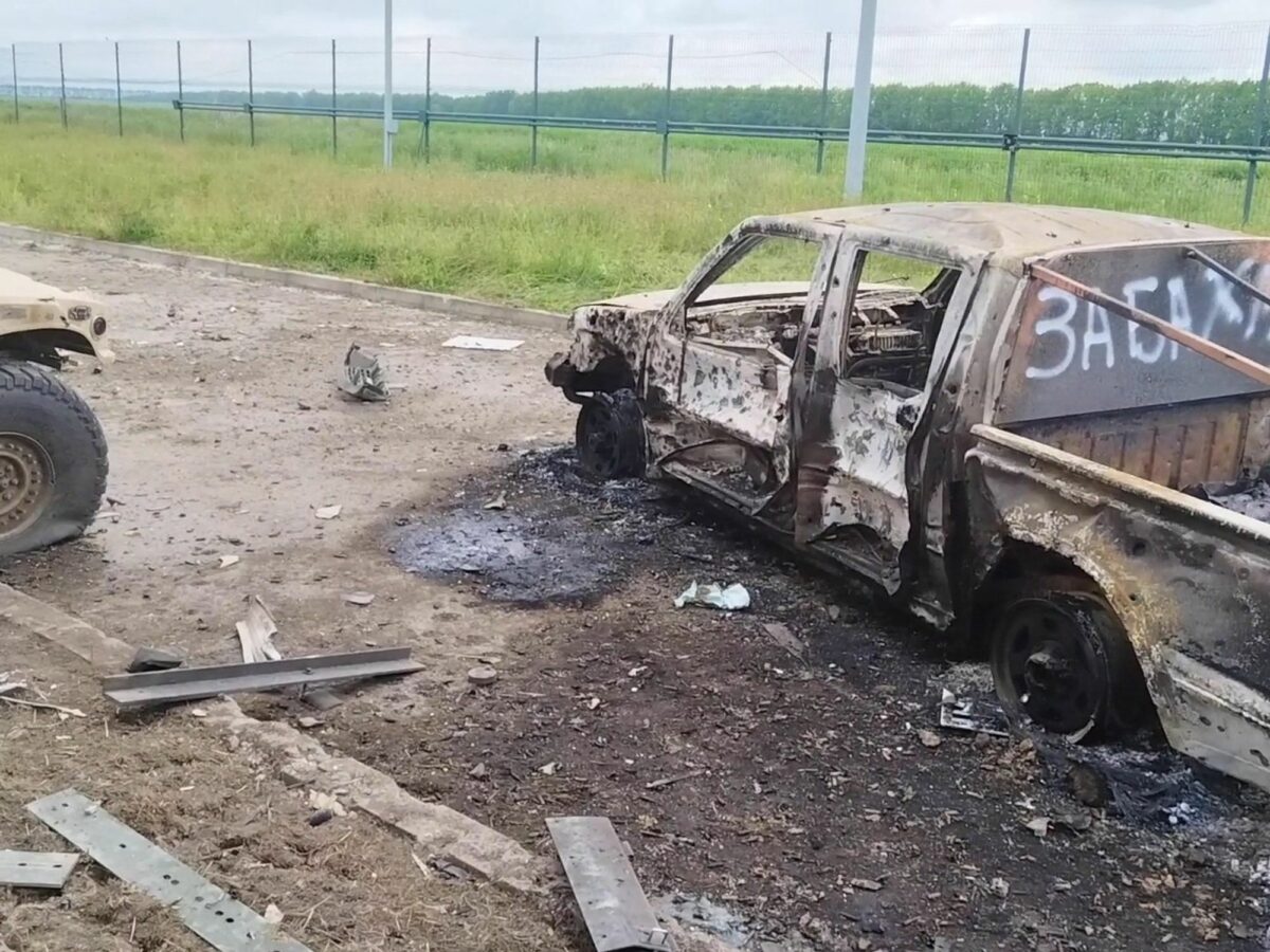 Burnt vehicules with white graffiti sit on a dirt road