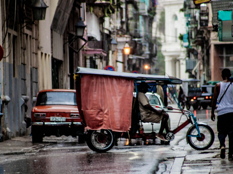 cars, buggies, and people travel through the streets of downtown Havana.