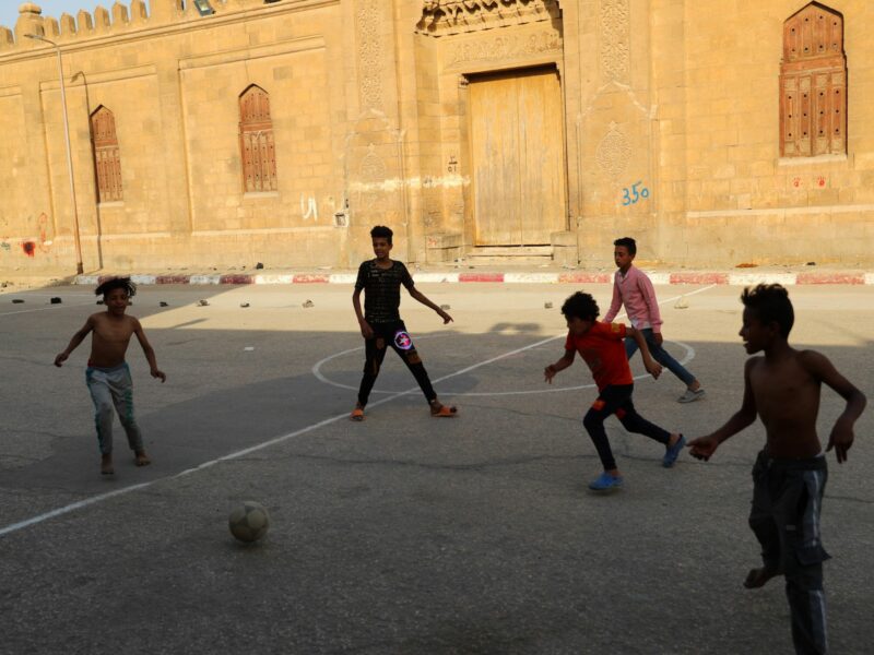 Children play football on an open space at a slum area with cemeteries