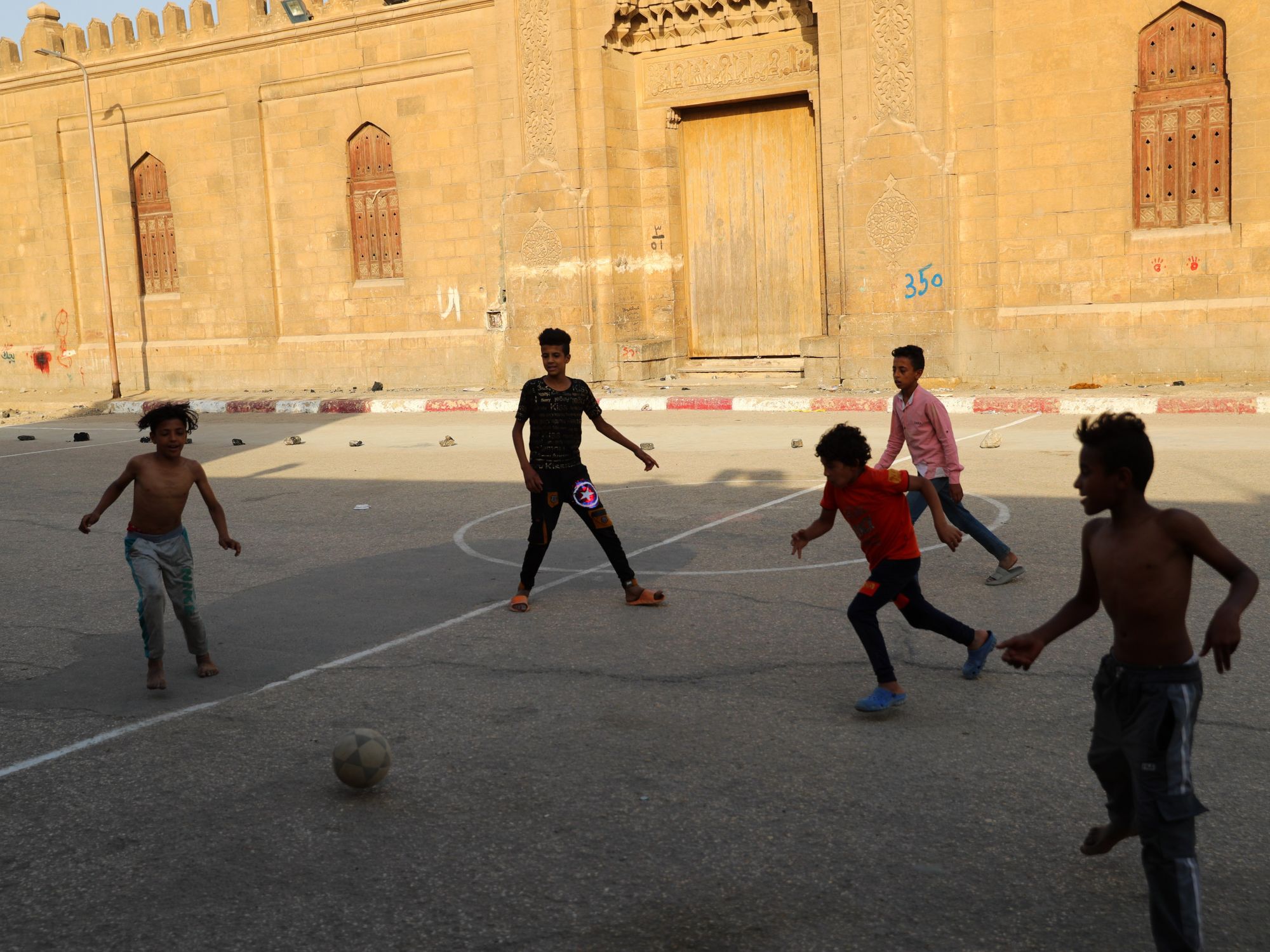 Children play football on an open space at a slum area with cemeteries
