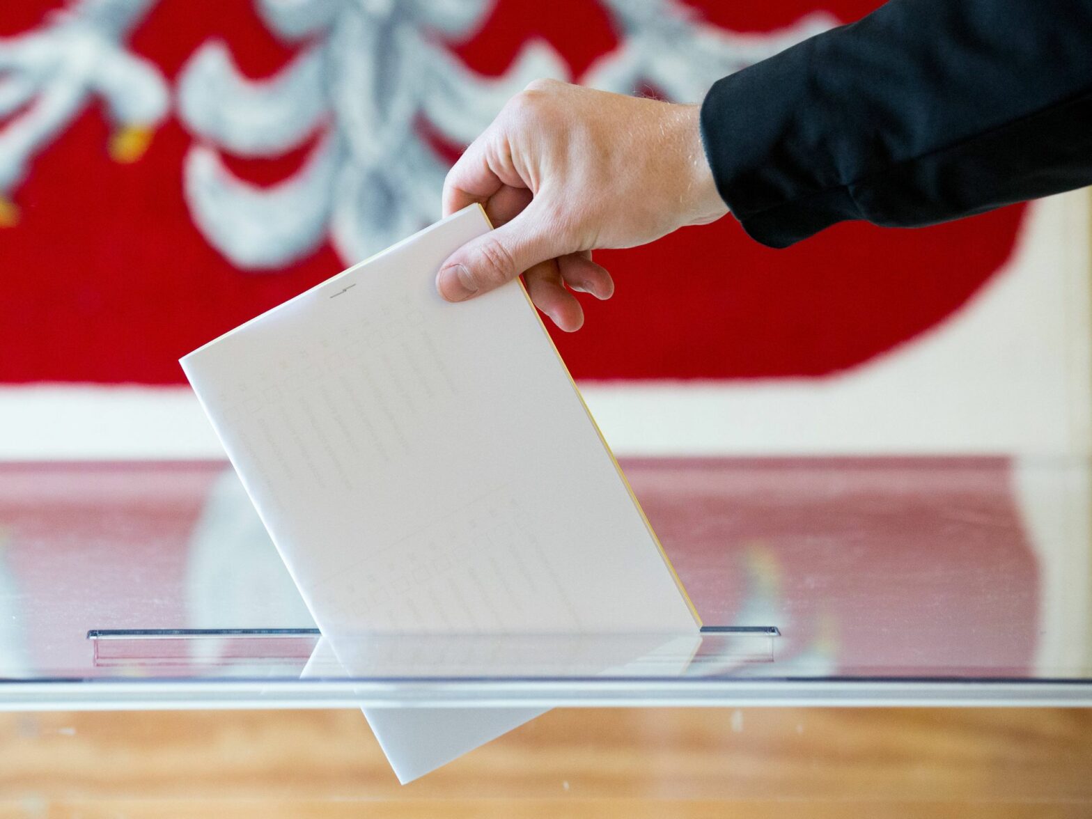Close up on a hand putting a vote in a ballot box, with the Polish flag as backdrop