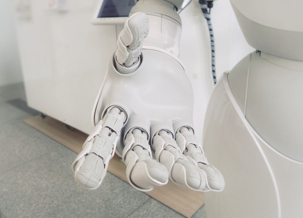 Close-up photo of a white robot hand reaching toward the camera, palms open.