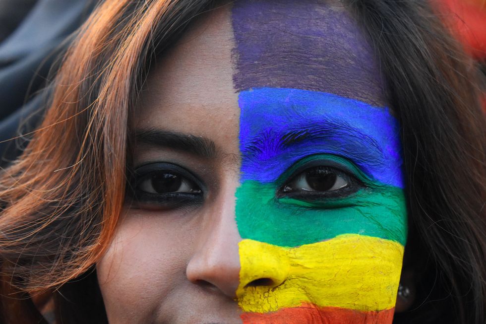 Close-up photograph of a woman's face half covered in rainbow make up, celebrating pride in India.