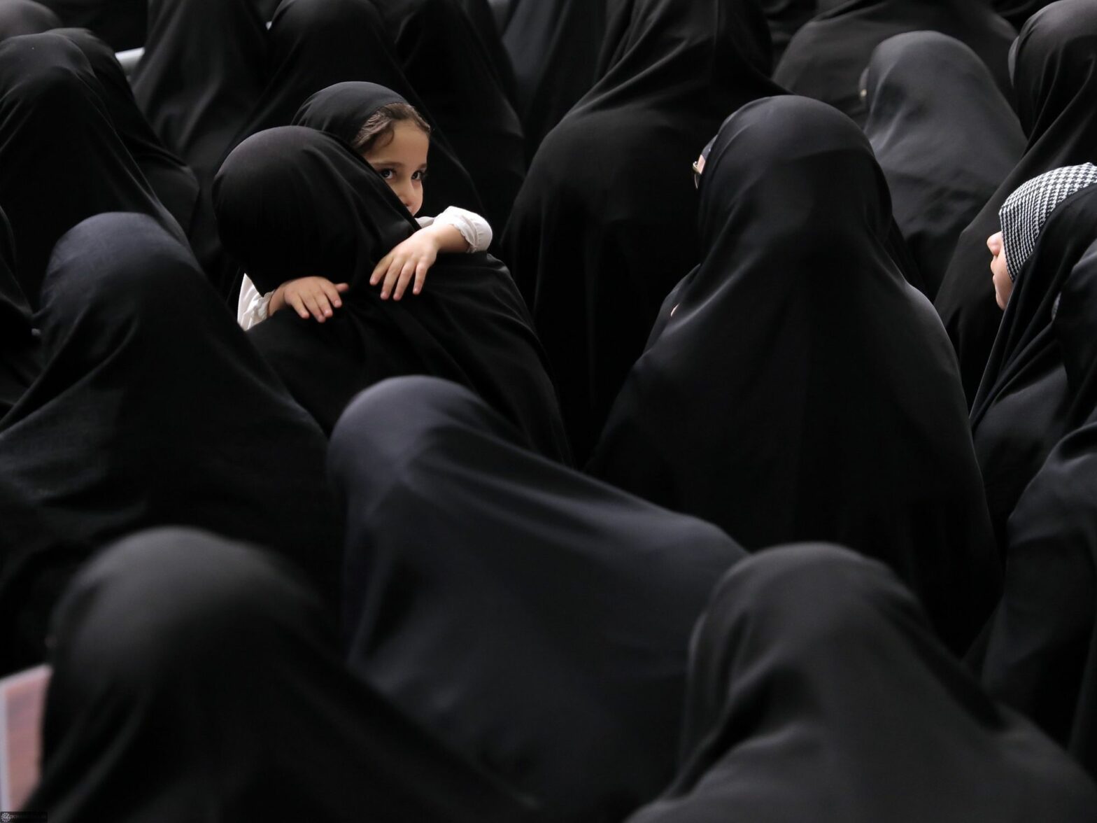 Crowd of women wearing hijab while a small child is being carried also wearing a hijab