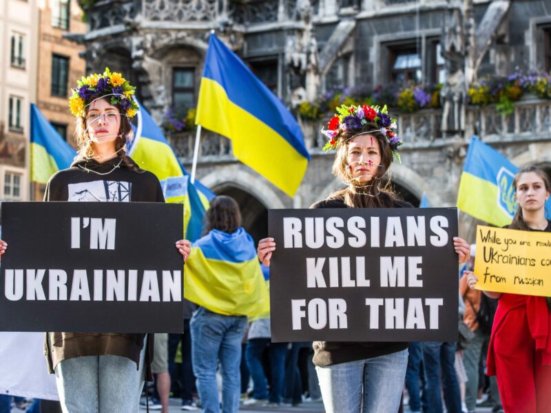 Demonstrators against the war wearing sunflowers. One has a sign that says "I'm Ukrainian" and the other has a sign thatt says "Russians kill me for that"