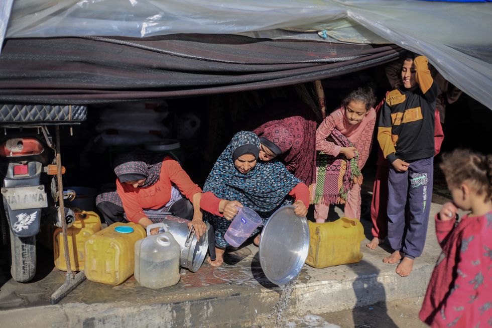 Displaced Palestinian women from the north of Gaza City clean cooking pots outside a temporary tent established on the sidewalk on a street in Rafah because there is no room for them in the camp areas.