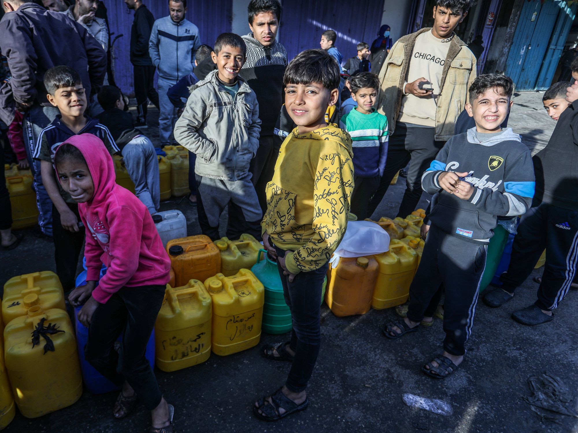 Displaced Palestinians stand in queue to fill bottles and jerrycans with water.
