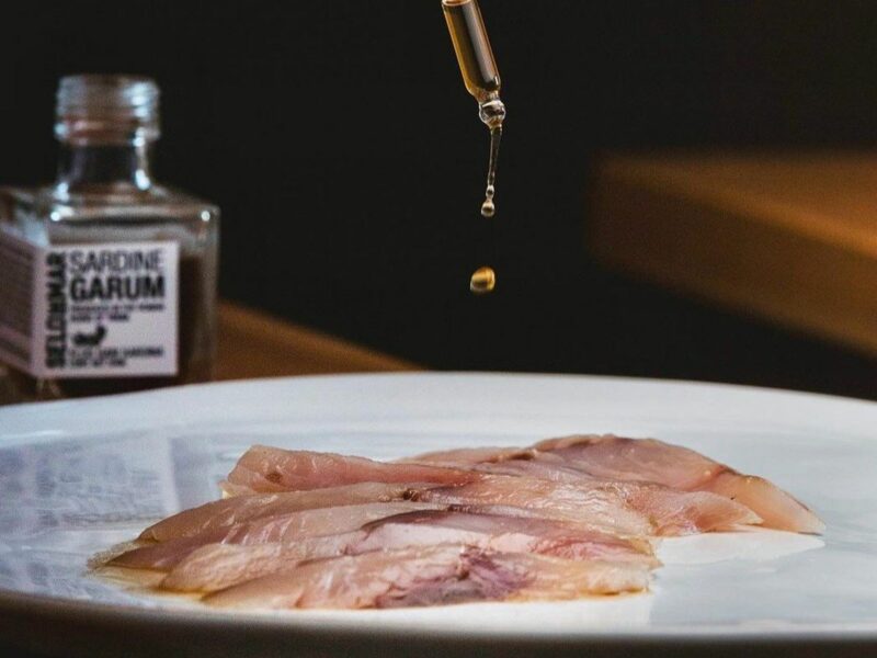Dropping some Garum, a special sardine-based sauce, on a plate of fish.