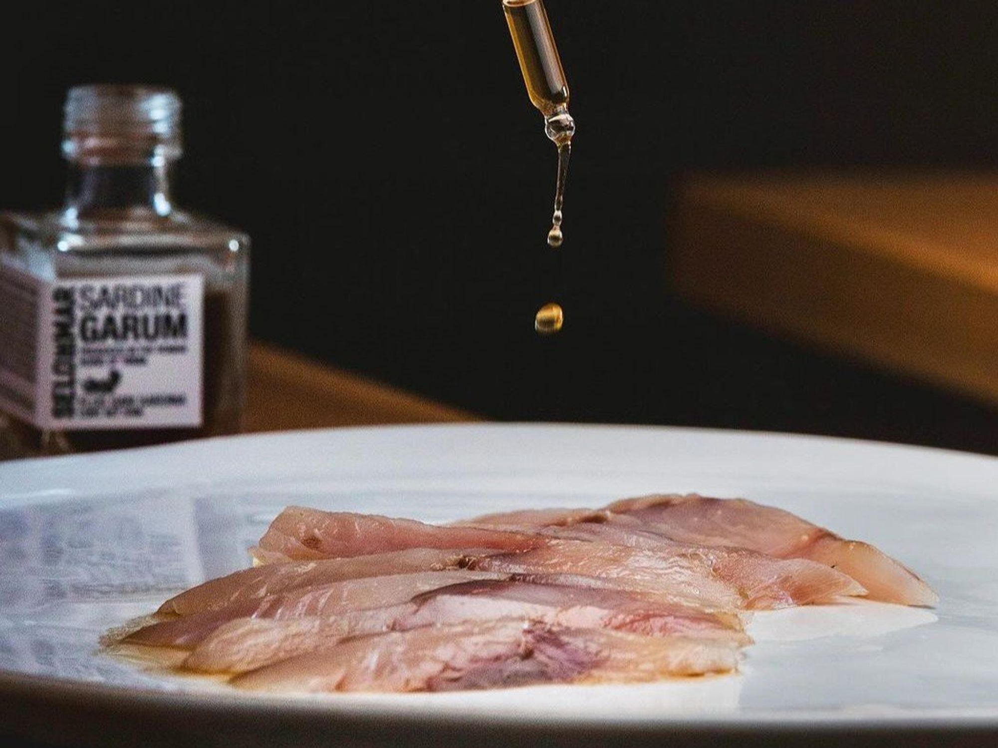 Dropping some Garum, a special sardine-based sauce, on a plate of fish.