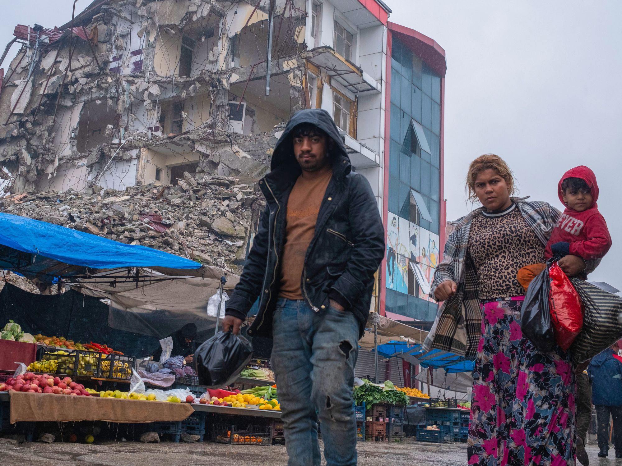 ​A family shops at the market set up on the street of demolished houses in Hatay, Turkey.