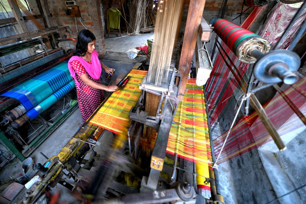 ​A female worker on a handloom machine to produce fibres which will then be used to make a Saree, the Indian traditional dress, in West Bengal, India, in January 2021.