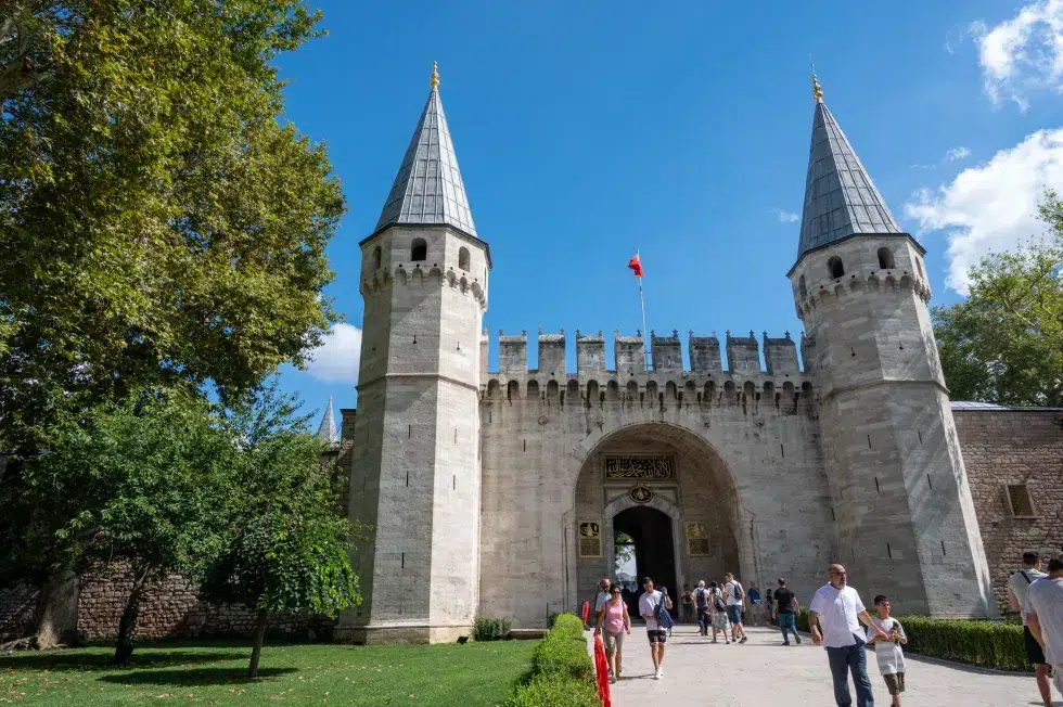 ​A group of people walking outside of a castle with Topkapı Palace in the background.