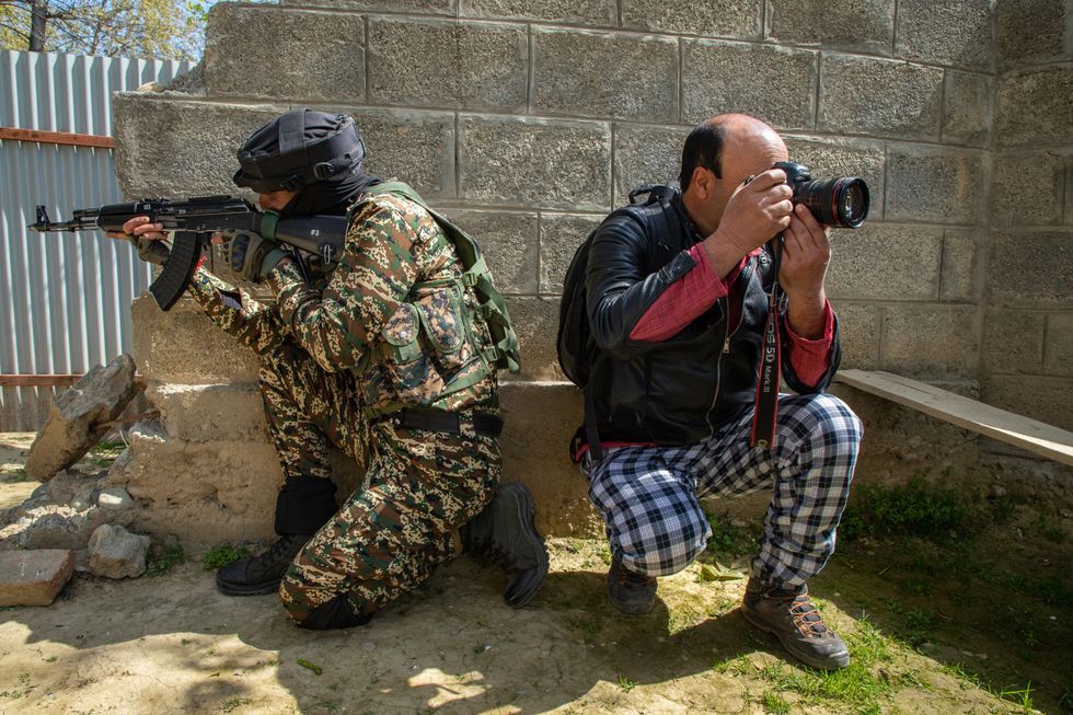 ​A Kashmiri photojournalist seen taking pictures as Indian army soldier takes position.