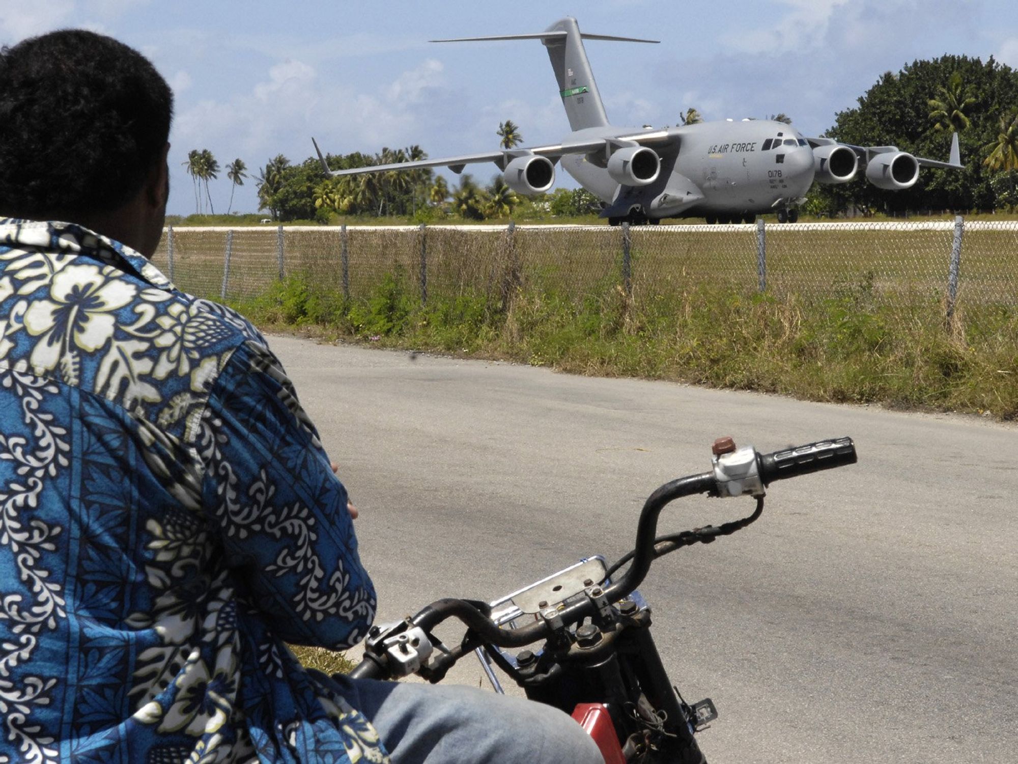 ​A local man from Nauru on a motor bike watches as an American aircraft lands
