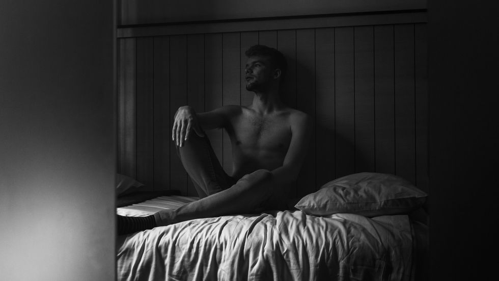 ​A man sits in bed alone pondering.
