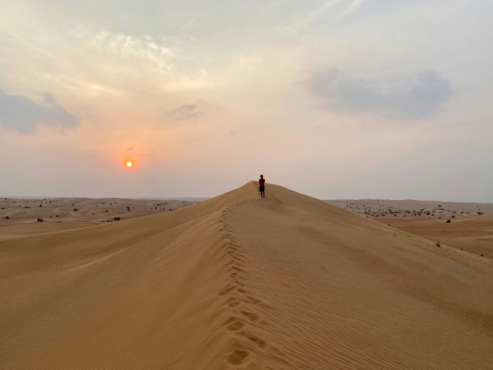 ​A person walking on the brown sand dunes of Dubai during day time.