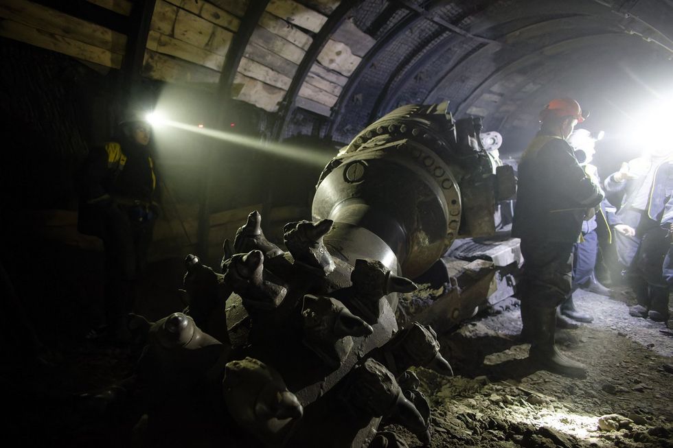 ​A photo of an underground drill on display with miners standing around it.
