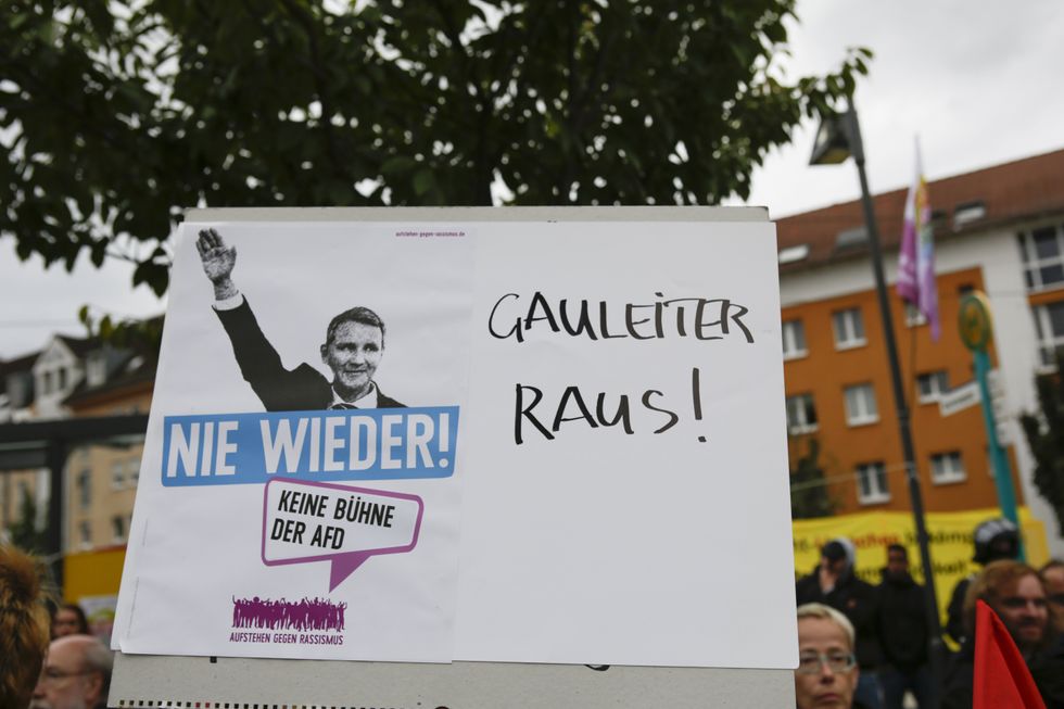 ​A protester holds up a sign that has a picture of AfD politician Bjorn Hocke making a Nazi Salute and written 'Never again' and 'Gauleiter out'.