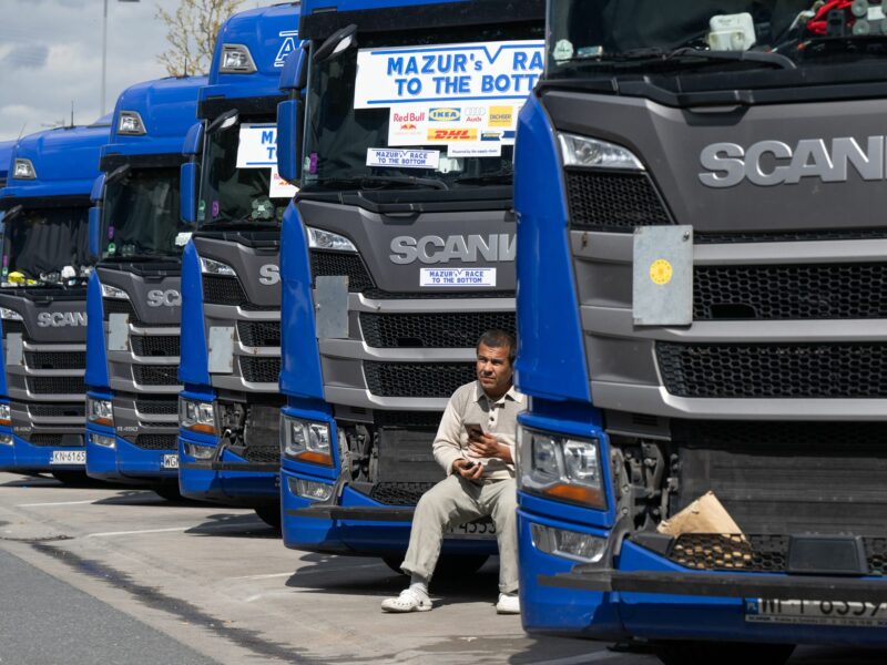 ​A trucker sits in front of the grille of his truck at the rest stop.