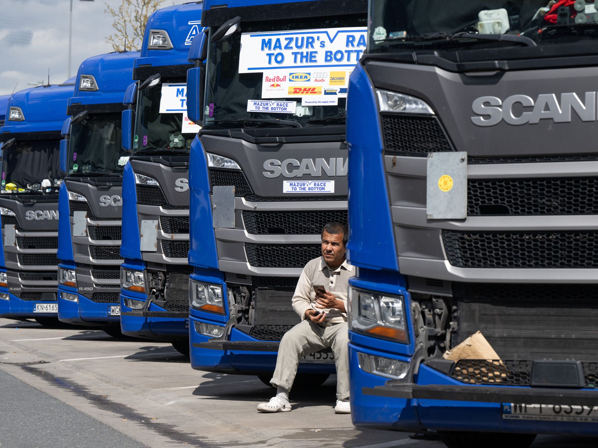​A trucker sits in front of the grille of his truck at the rest stop.
