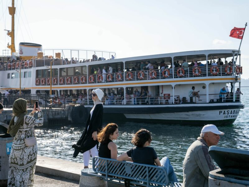 ​A woman poses for a photo in front of a ferry on the coast of Istanbul on June 21, 2024.