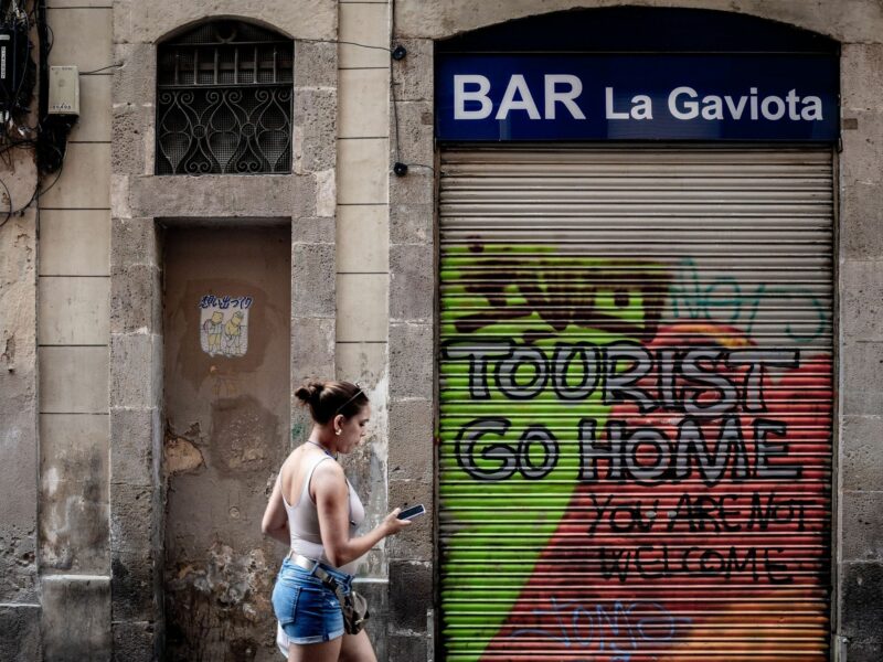 ​A woman walks past an anti-tourism graffiti reading ''Tourists, go home'' in Barcelona, Spain amidst protests against mass tourism in anticipation of a record number of visitors in 2024.