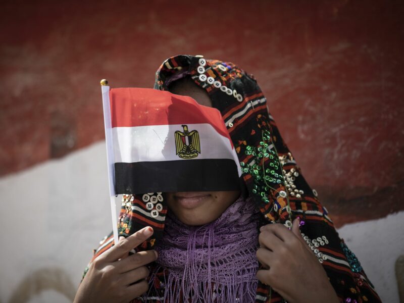 ​A young girl in Egypt in Siwa, Egypt covers her face with the nation's flag.