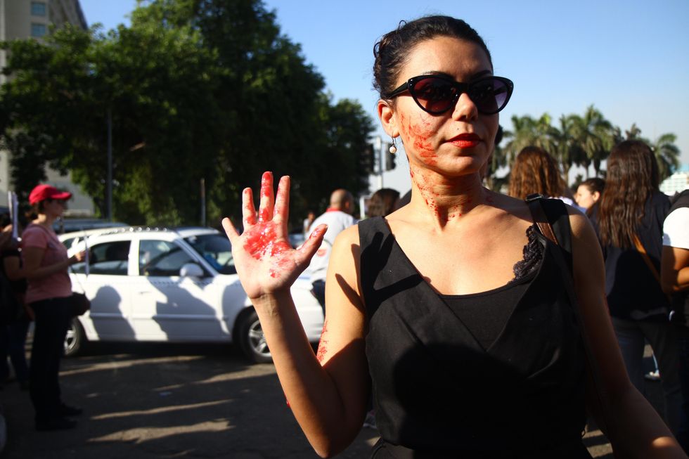​An Egyptian woman with red paint on her face and hand depicting blood during a protest against sexual harassment in Cairo.