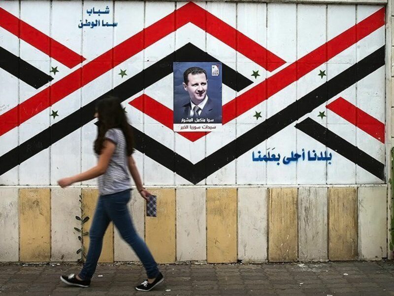 ​Assad poster in Damascus as a woman walks by.