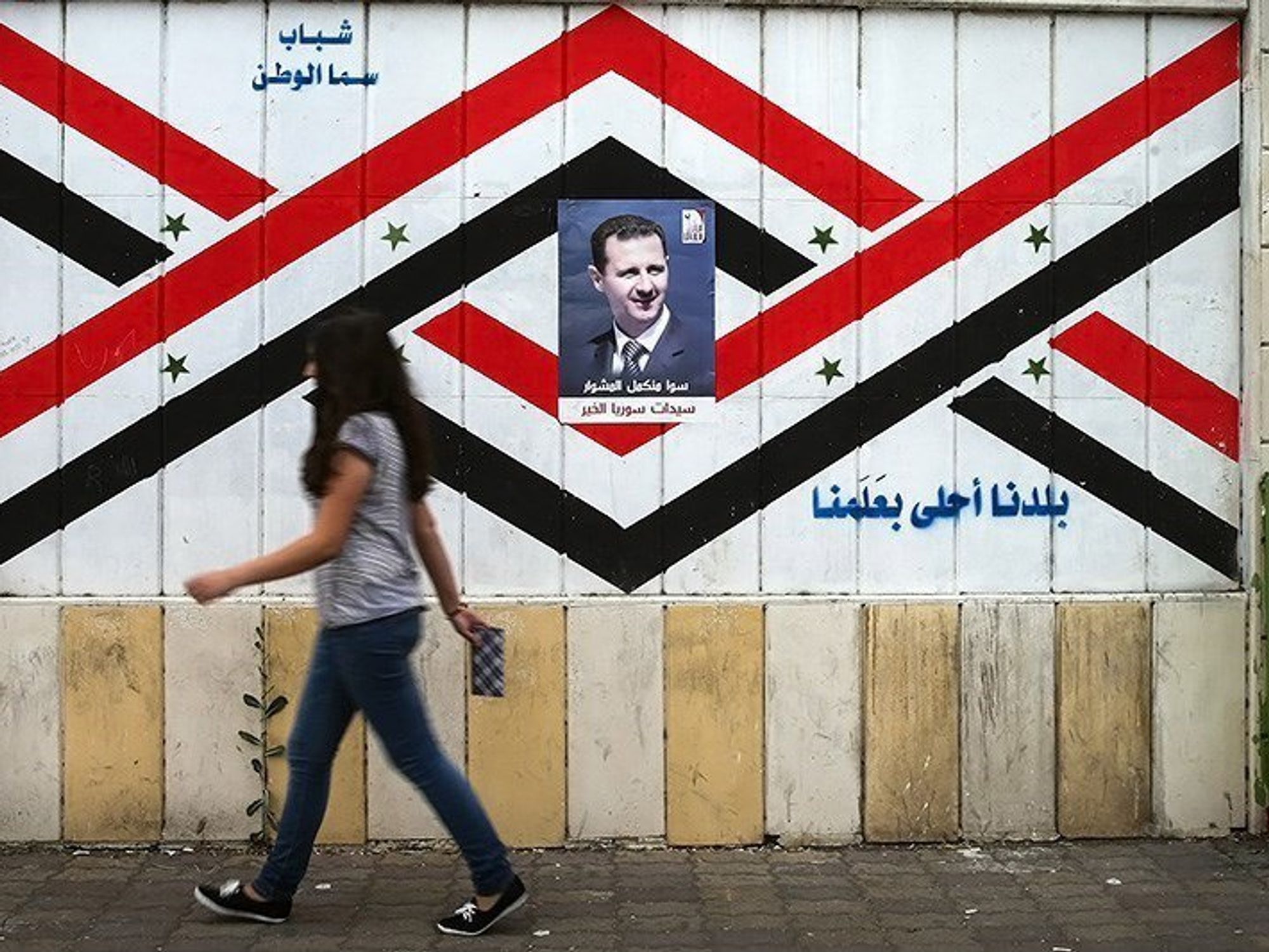 ​Assad poster in Damascus as a woman walks by.