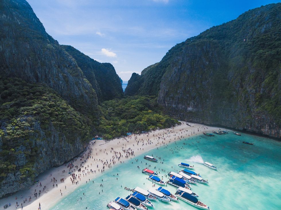 ​Bird's eye view photography of Maya Bay, with ships moored on the shore and people standing around the beach.