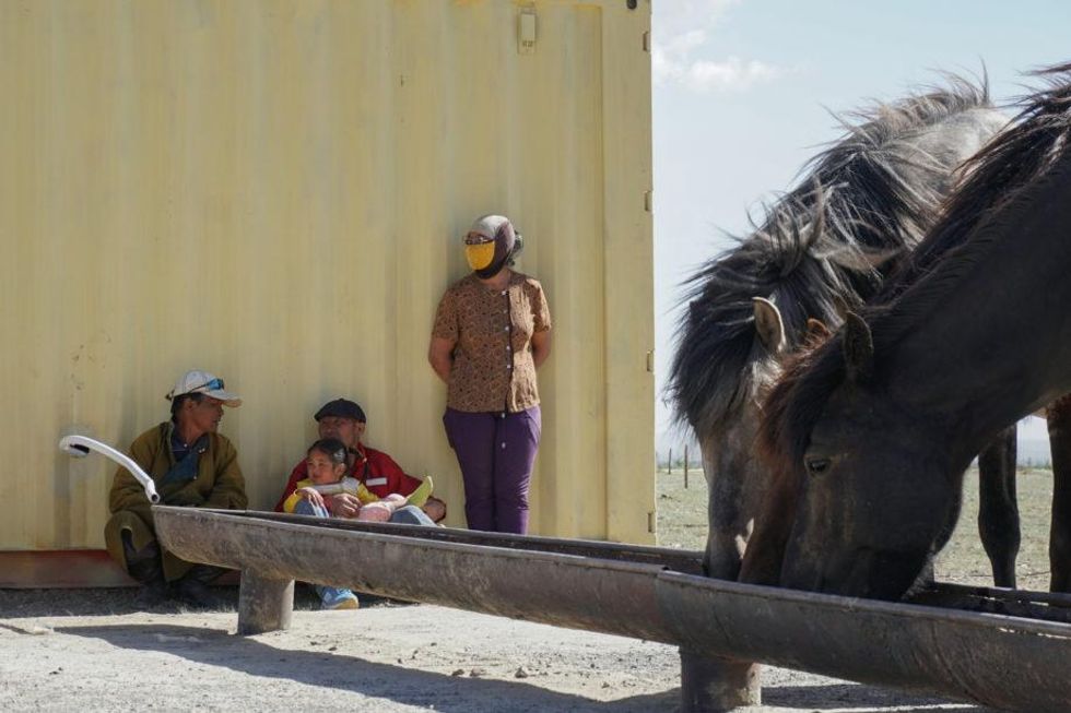 ​Bolortuya Bekh-Ochir, Batbaatar Tsedevsuren, with their daughter Tuvshinkhishig Batbaatar, and Battumur Ayaakhuu rest in the shade while Battumur’s herd drinks water.