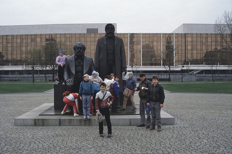 ​Children play by the statues of Marx and Engels at the Marx-Engels-Forum, in the Mitte district of former East Berlin. It's April 1989, around six months before the fall of the Berlin Wall. The huge, modernist building in the background has been demolished too: the "Palast der Republik" (Palace of the Republic), the parliament of the German Democratic Republic, was torn down in 2006.