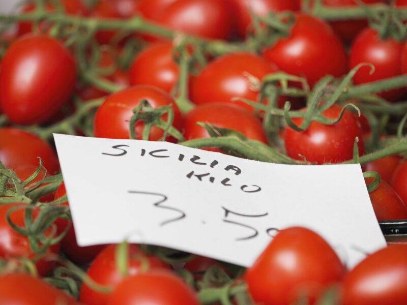 ​Close up of a market stall and fresh produce. Tomatoes on the vine, and a price label.