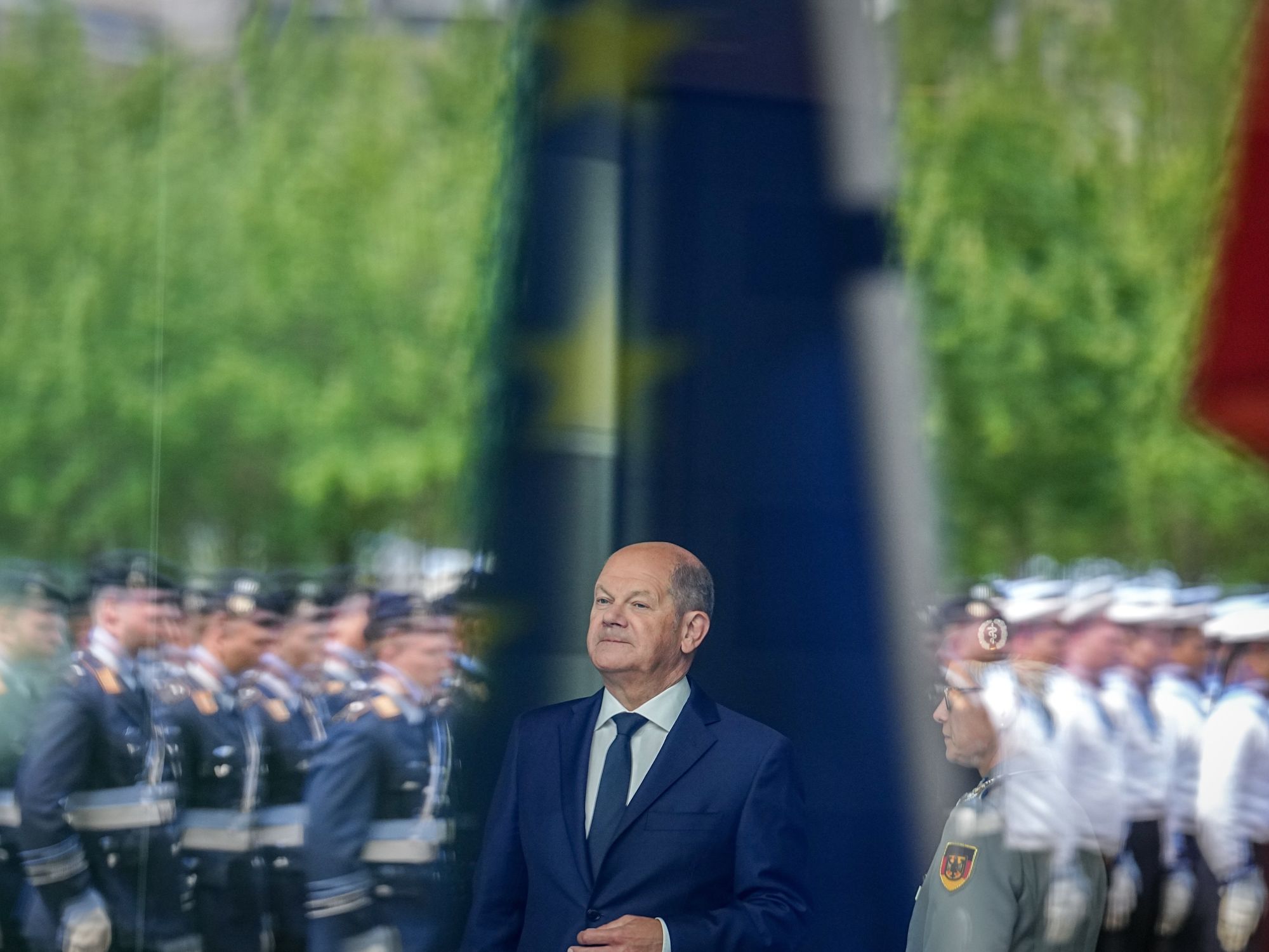 ​Federal Chancellor Olaf Scholz stands waiting amongst German soldiers.