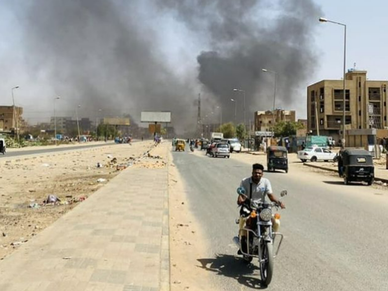 ​Image of a man on his motorcycle in Khartoum, Sudan, driving away from smoke.