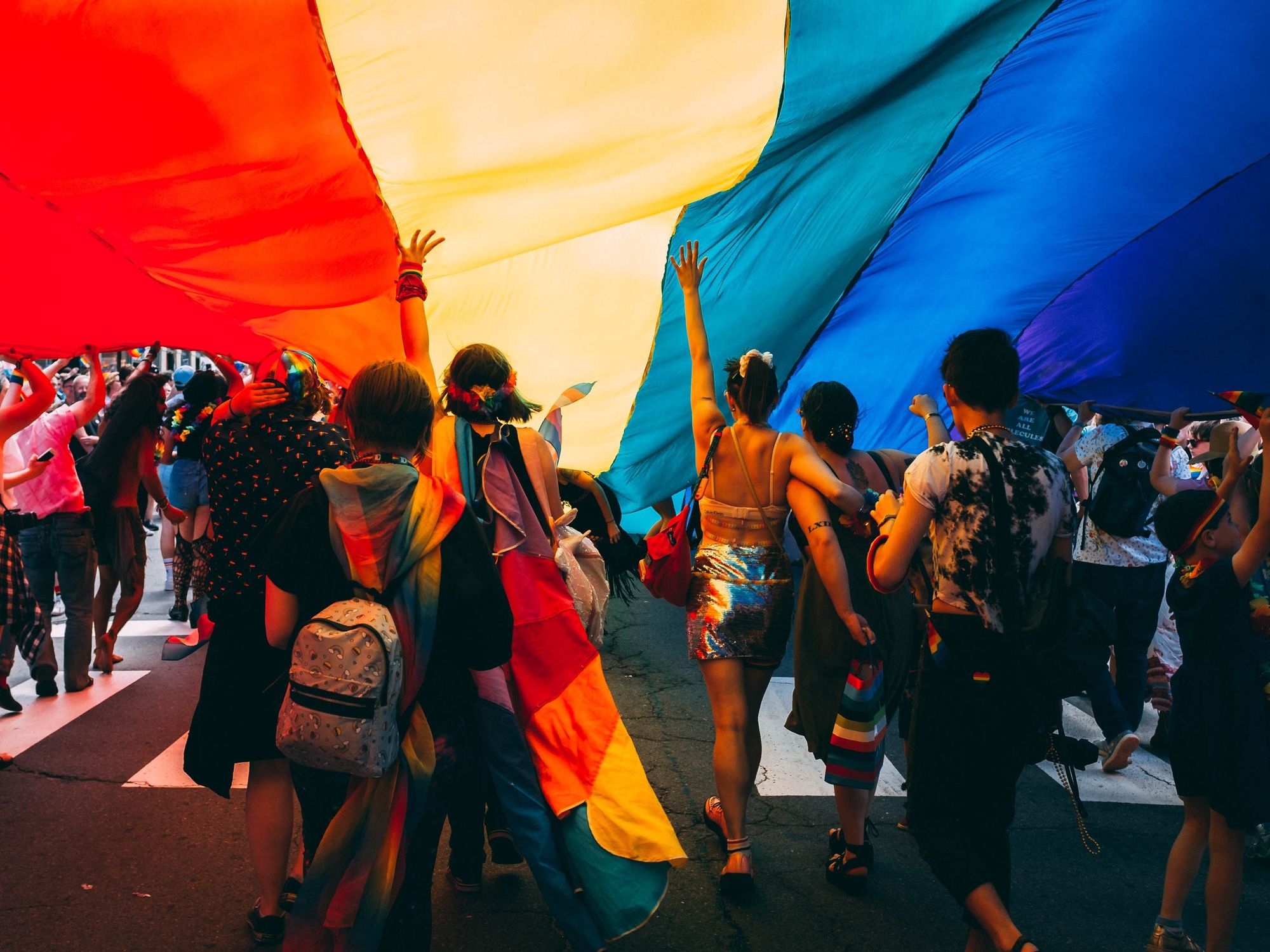 ​Image of people marching under the LGBTQIA+ flag during a demonstration.