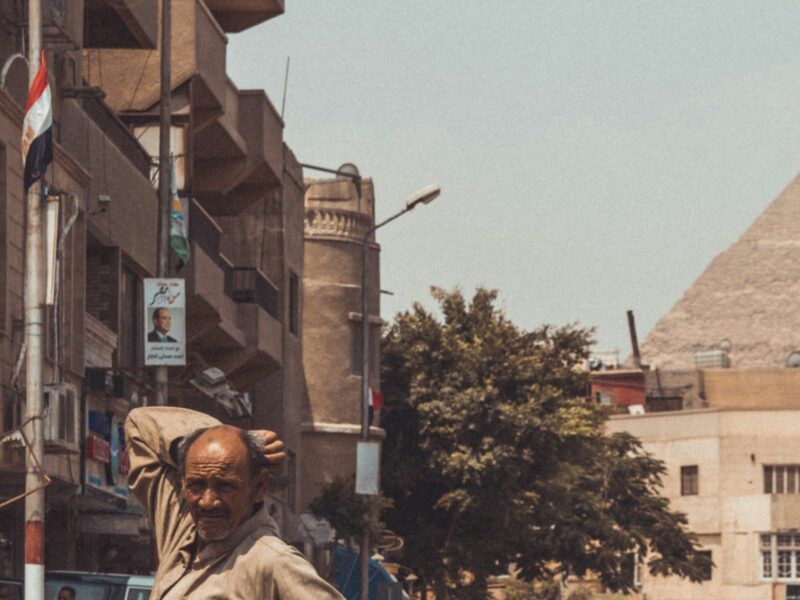 ​Man in brown throbe stands in front of the pyramids.