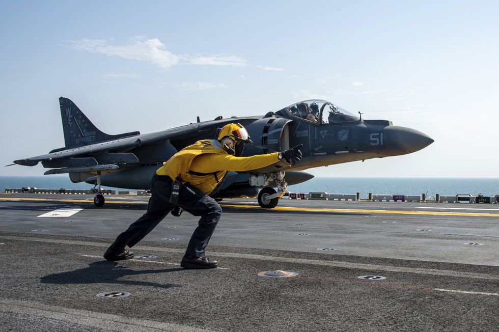 ​Navy sailor signals a Marine Corps AV-8B Harrier fighter aircraft for take off in the Arabian Sea.