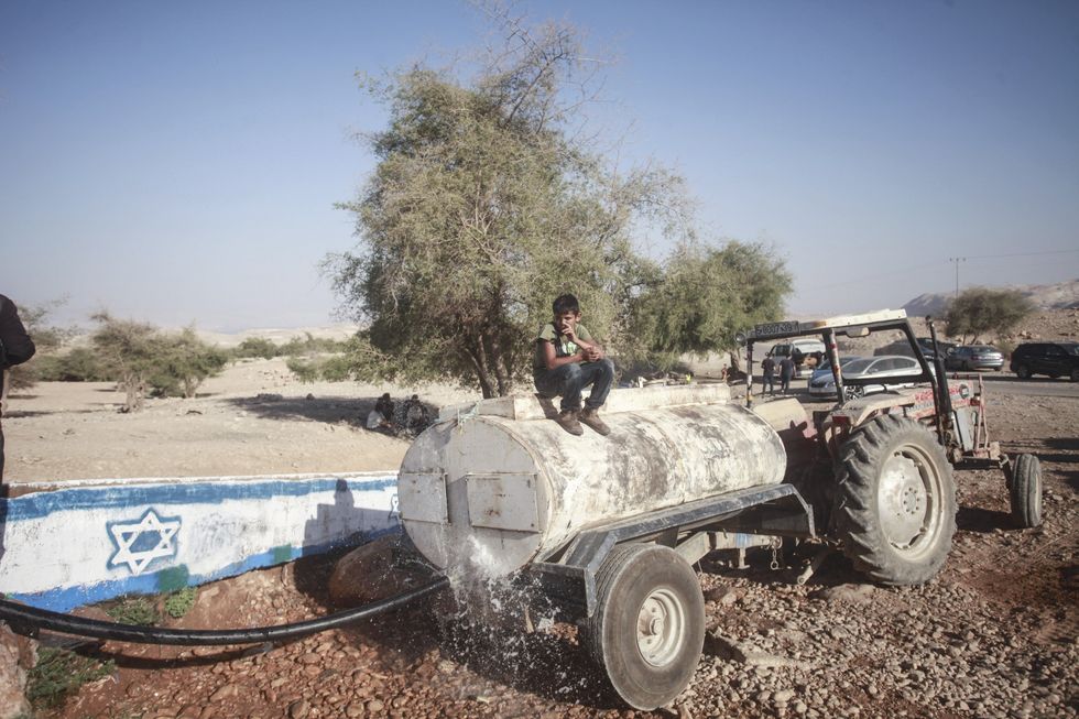 ​Palestinians fill their tanks with water from the Uja River canal marked with an Israeli flag by Jewish settlers near Jericho. In the last year, illegal Israeli settlements in the West Bank have been expanding dramatically, with settlers reclaiming more and more of the land and its resources; July 17, 2024.