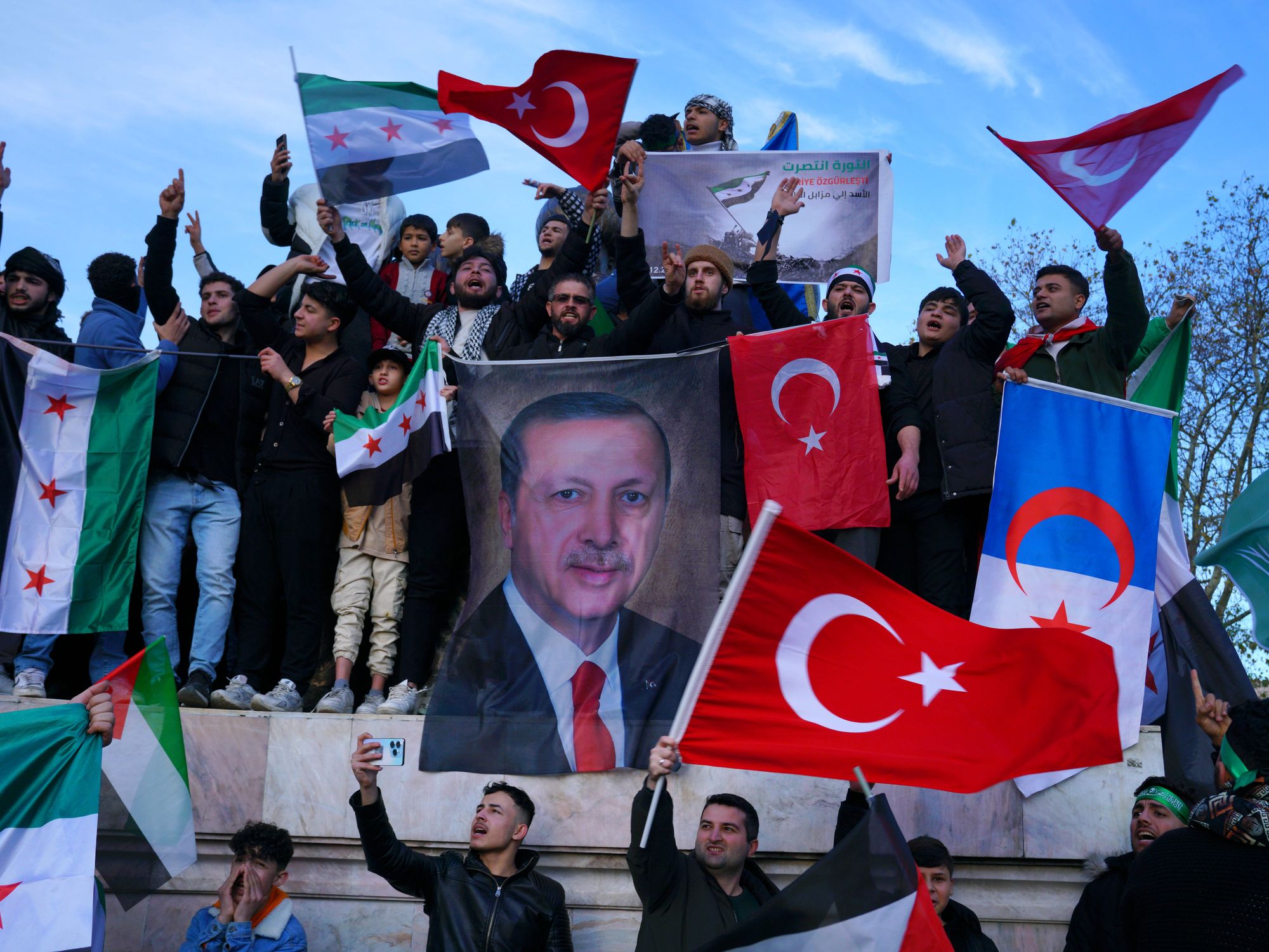 ​photo of Syrians living in Turkey holding a large poster of Turkish President Recep Tayyip Erdogan after Syrian rebels announced that they have ousted President Bashar al-Assad, at Sarachane Square in Istanbul, Turkey, Dec. 8, 2024.