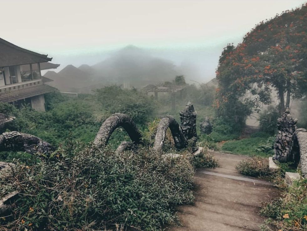 ​Photograph of the Ghost Palace Hotel taken on a misty day. It looks down on the mountain, with complex dragon-like statues weaving around the steps