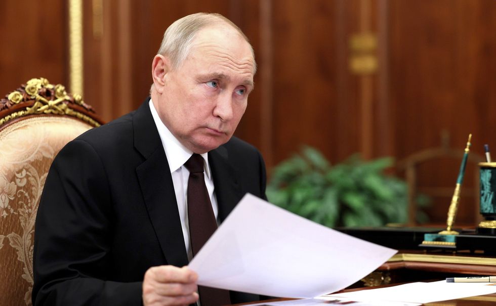 ​Russian President Vladimir Putin shuffling papers while listening.