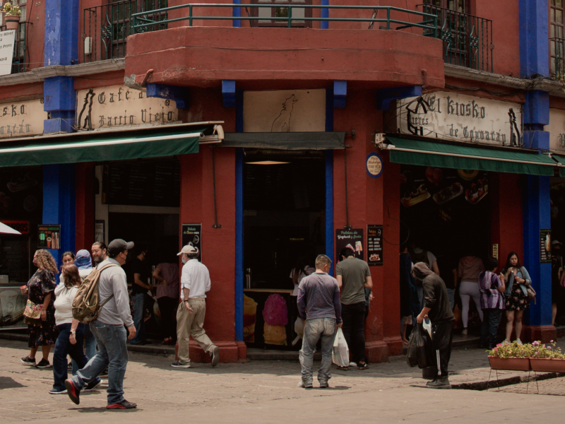 ​Street scene showing people walking by a red building in Coyoacán, Mexico City